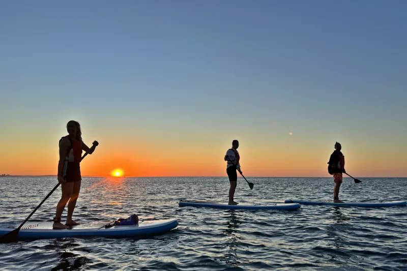 A stand-up paddleboarder on calm water at sunrise near Lagos
